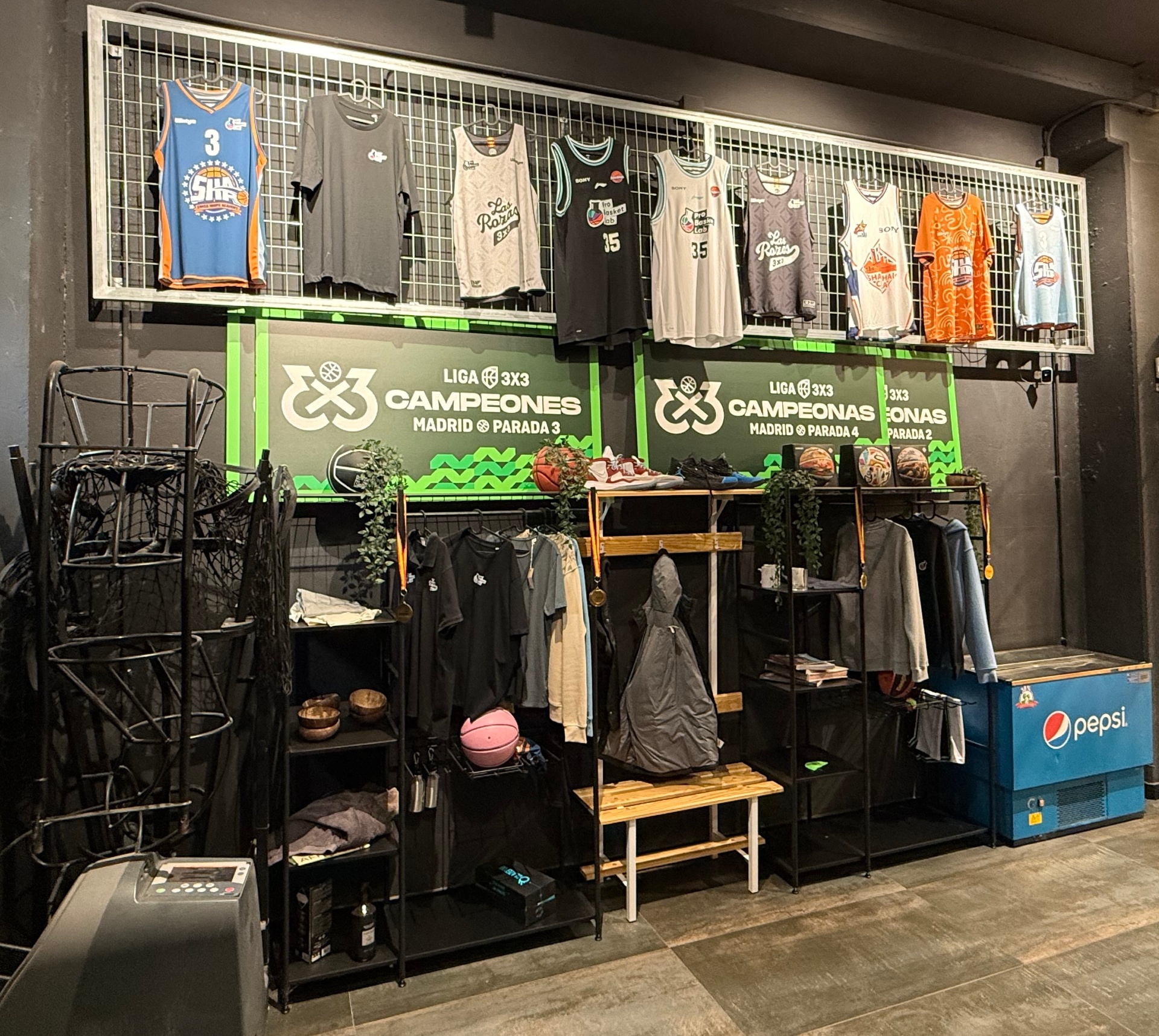 Pared de merchandising PBL con camisetas de equipos, banners de campeones 3x3 y ropa del club